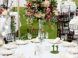 a refined wedding table setting with neutral linens, tall bold floral centerpieces and greenery, moss table numbers and gold chargers plus string lights