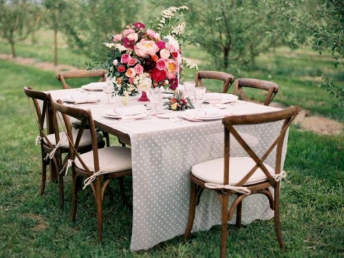 a bright and chic wedding tablescape with a polka dot tablecloth and neutral napkins, a bold and lush floral centerpiece and neutral place settings for a summer backyard wedding