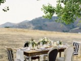 a refined backyard wedding tablescape with a white runner, with elegant vintage chairs, a greenery and white bloom wedding centerpiece and candles