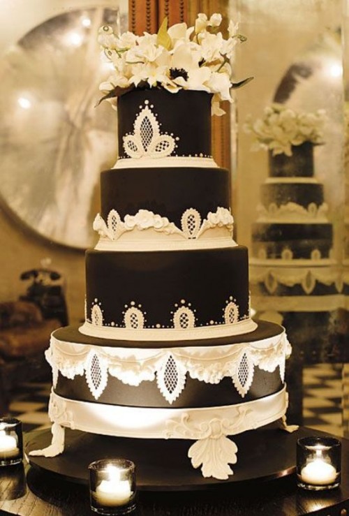 an exquisite vintage black wedding cake with white lace and sugar patterns, white blooms and gold leaves on top for a refined and chic wedding