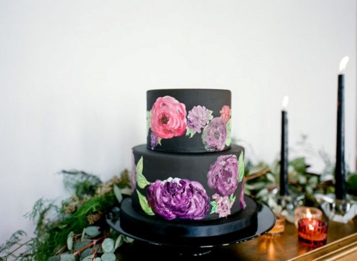 a plain black wedding cake with colorful painted blooms on it is a very chic and bold idea for a modern wedding with bright blooms