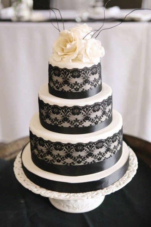 a white wedding cake with black lace and black ribbon, with white blooms and black twigs on top is a classic idea for a vintage wedding in a monochromatic color scheme