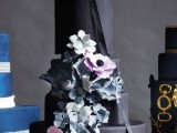 a matte black wedding cake with black ribbon, with pastel blue and pink sugar blooms is a refined and chic idea for a dark romance or Halloween wedding