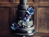 a sleek and plain wedding cake with black ribbons, with blue, green and purple sugar blooms is a stylish idea for a moody wedding with a touch of color