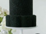 a black wedding cake with a touch of glitter and a white and black flower is a stylish idea for a contrasting black and white wedding