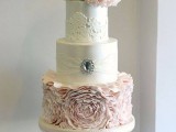 a white and blush wedding cake with a ruffle flower tier, lace and a brooch with a rhinestone plus large blush sugar blooms on top