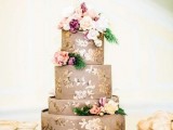 a taupe wedding cake with gold floral patterns, fresh blooms and greenery on top for a chic and refined look