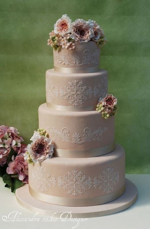 a blush wedding cake with white lace decor, creamy ribbons and some fresh blooms and greenery