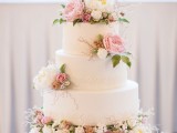 a white wedding cake with lace decor and lots of fresh blooms in pink and white and greenery