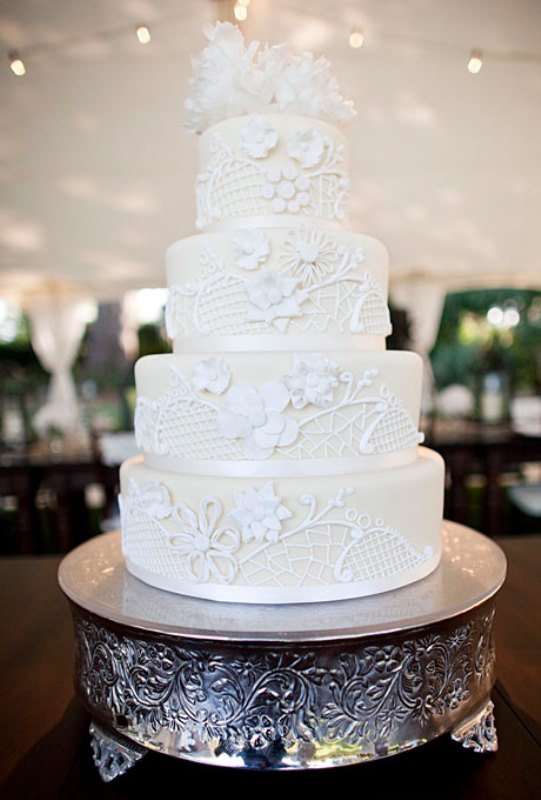 An ivory wedding cake with white lace decor and sugar blooms on top is vintage style classics