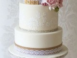 a neutral rustic vintage wedding cake with white lace, burlap ribbons, scrabble letters, pink and white sugar blooms and wooden toppers