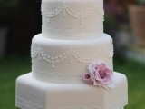 a white vintage wedding cake with patterns, pink sugar blooms on top for a refined touch