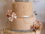 a tan wedding cake decorated with white floral patterns, ribbons, embellishments, tan sugar blooms is a glam idea