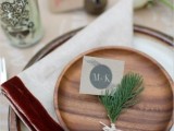 a rustic wedding tablescape with a porcelain charger, a wooden plate, twigs of greenery and blooms and bells around for a fall to winter wedding