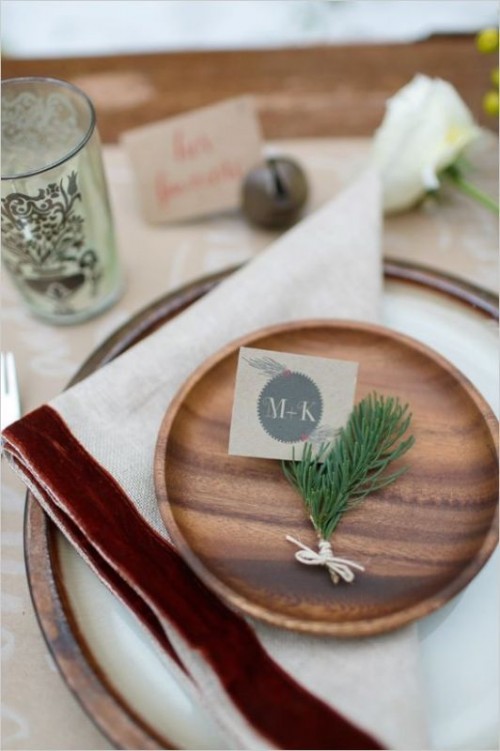 a rustic wedding tablescape with a porcelain charger, a wooden plate, twigs of greenery and blooms and bells around for a fall to winter wedding