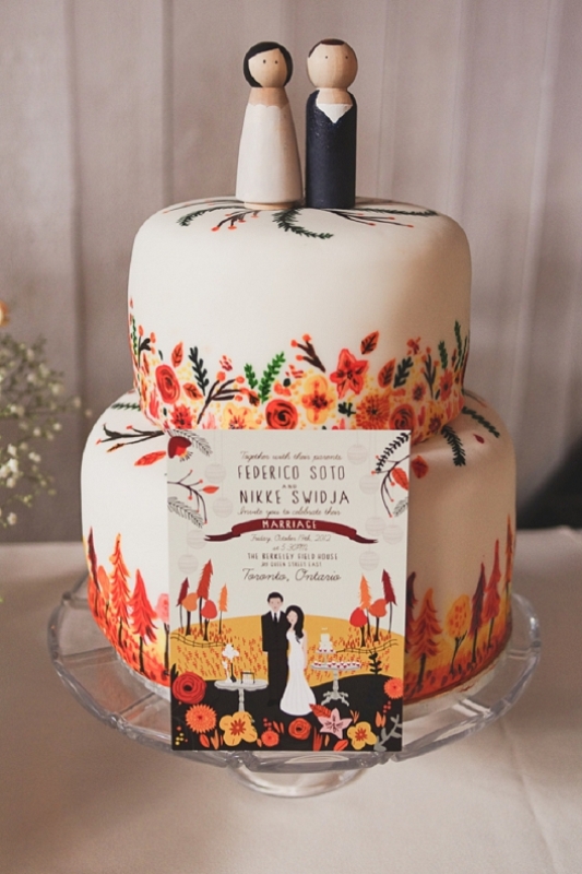 a white wedding cake with colorful blooms and trees painted on it and with kokeshi doll cake toppers is a lovely idea for a bright wedding