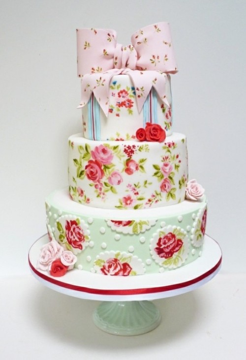 a creative floral wedding cake with all-mismatching painted tiers, and with a sugar floral pink bow on top is a lovely idea