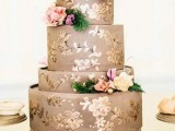 a taupe wedding cake painted with gold flowers and topped with pastel and neutral blooms and greenery is a refined and elegant idea for a wedding