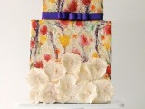 a unique square colorful and textural wedding cake with painted blooms, a navy ribbon and white sugar blooms attached is an amazing idea for a summer wedding with bright shades