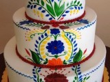 a white buttercream wedding cake with painted bright blooms and leaves done in boho and folk style, ideal for a Mexican wedding