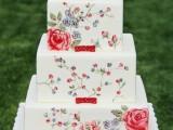 a square white wedding cake with bright painted flowers and a bit of greenery plus tiny red ribbon bows is a bold idea for a summer wedding