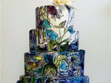 a dark-colored wedding cake with green and navy painted blooms in Monet style and a white sugar bloom on top is amazing