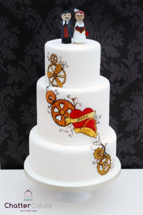 a white buttercream wedding cake with painted gears, a heart and names plus fun kokeshi doll cake toppers