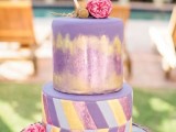 a purple wedding cake with gold hand painting and lovely yellow, pink and purple chevron detailing and fresh pink blooms for a colorful wedding