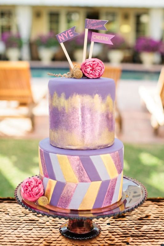 a purple wedding cake with gold hand painting and lovely yellow, pink and purple chevron detailing and fresh pink blooms for a colorful wedding