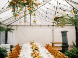 a colorful indoor spring wedding reception with lights, blooms and greenery hanging over the tables and matching blooms on the tables