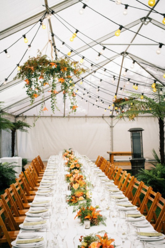a colorful indoor spring wedding reception with lights, blooms and greenery hanging over the tables and matching blooms on the tables