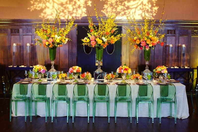 a bright spring wedding reception with colorful arrangements in tall green vases, green chairs, bright blooms