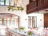 a refined indoor spring wedding reception with greenery on the chandelier, greenery and blooms on the tables and lots of natural light