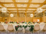 a spring wedding reception with greenery on the chairs and bright florals on the tables plus pendant lamps