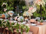 a lush outdoor spring wedding reception with lots of lush greenery, pastel blooms and tall candle holders