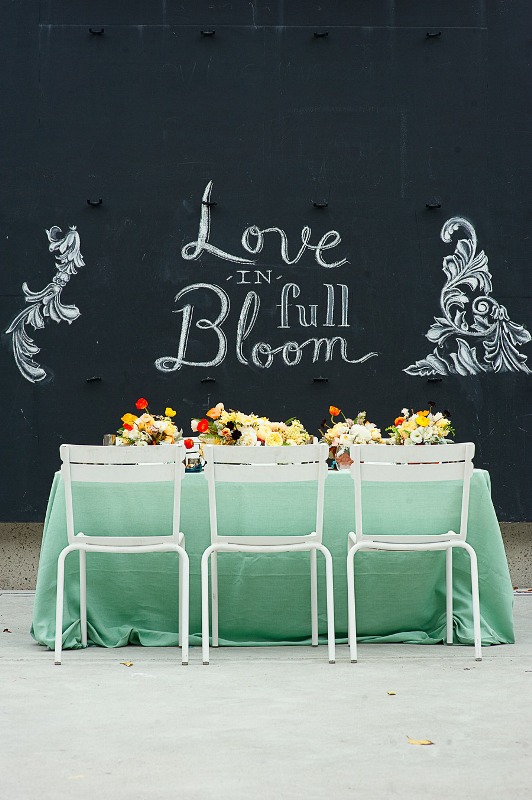 a bold spring wedding reception with a chalkboard wall, a mint tablecloth, bright blooms for centerpieces