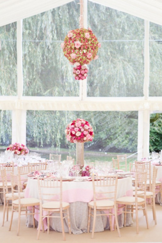 a chic indoor spring wedding reception with lush bright blooms over the tables and on them, pink tablecloths and pastel touches