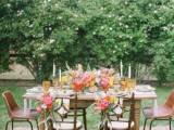 a bright outdoor spring wedding reception with colorful blooms, glasses and a boho rug under the table
