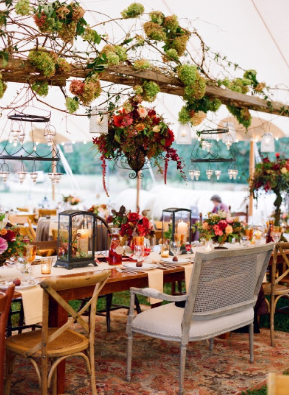 a super lush outdoor indoor spring wedding reception with lots of candle chandeliers, greenery, moss and bright blooms for a woodland feel