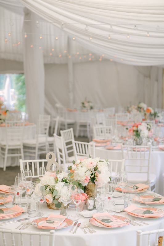 an indoor spring wedding reception in white, with pastel blooms and greenery, peachy chargers and monograms