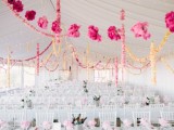 an indoor spring wedding reception with pastel and white bloom garlands hanging down, pink blooms on the tables and all white everything
