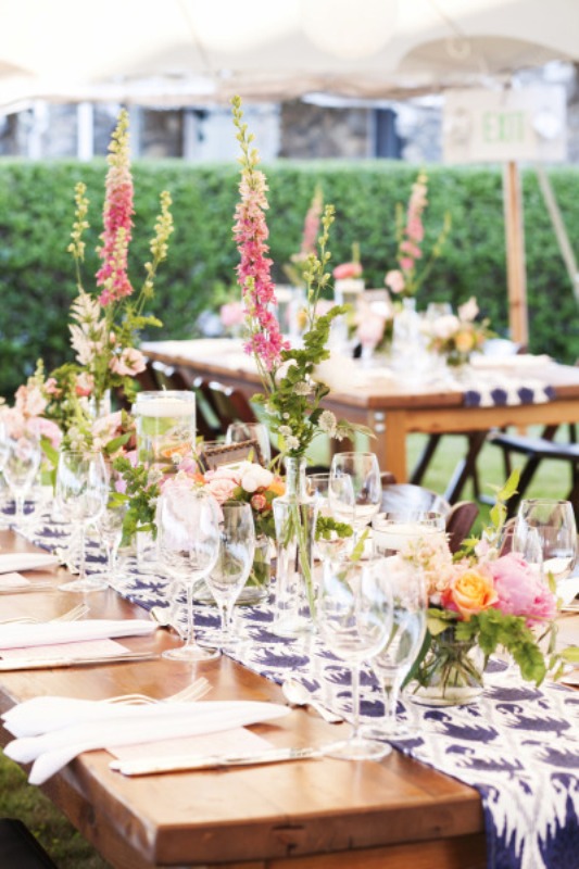a casual outdoor spring wedding reception with printed blue table runners, pink blooms and greenery on the tables