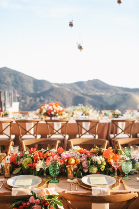 a colorful outdoor wedding reception done with bold blooms and greenery, some candles and colorful glasses