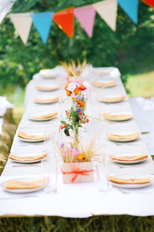a colorful outdoor spring wedding reception with colorful buntings, bright blooms, neutral linens and a white base