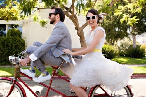 a retro-inspired ruffle knee wedding dress with a bright yellow sash and sunglasses for a cool bridal look