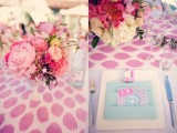 a pink and light blue wedding tablescape with lush florals, a napkin pocket and a bright printed tablecloth