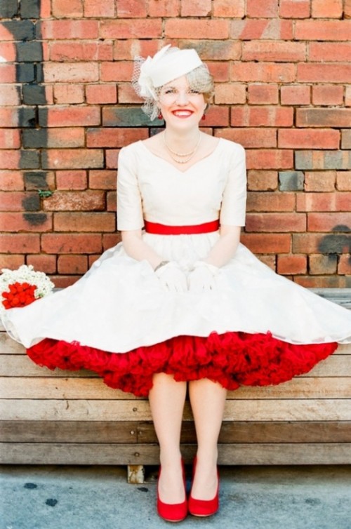 a retro midi wedding dress with a red sash and red underskirt, red shoes and pearls plus a birdcage veil