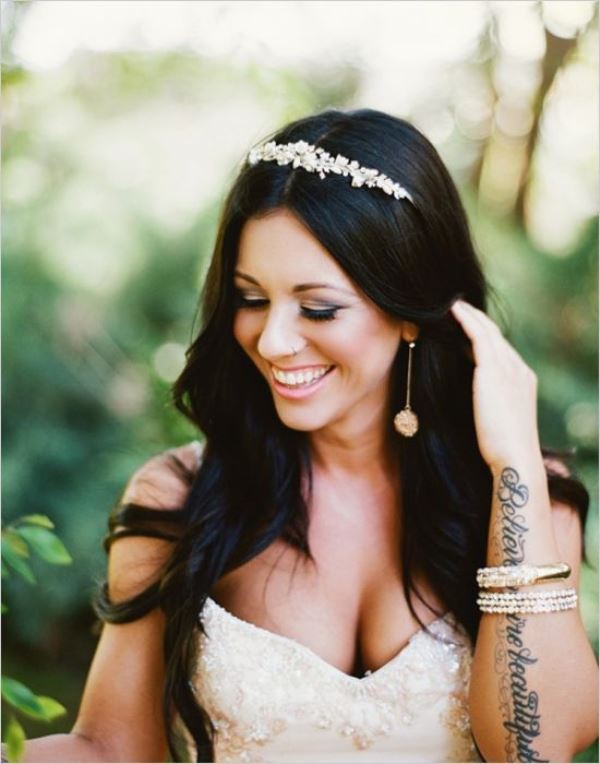 An embellished strapless wedding dress   absence of sleeves allows to see the bride's tattoos on her arm, and stacked bracelets accent the tattoo
