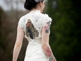 a beautiful fitting wedding dress of lace and with lace appliques, with a cutout back and short sleeves that show off the tattoos of the bride