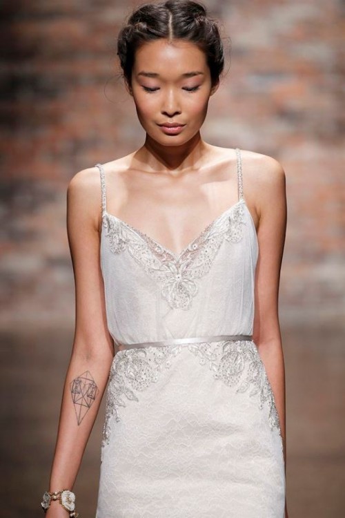 a delicate lace and plain wedding dress with embellishments shows off the bride's tattoos as there are no sleeves